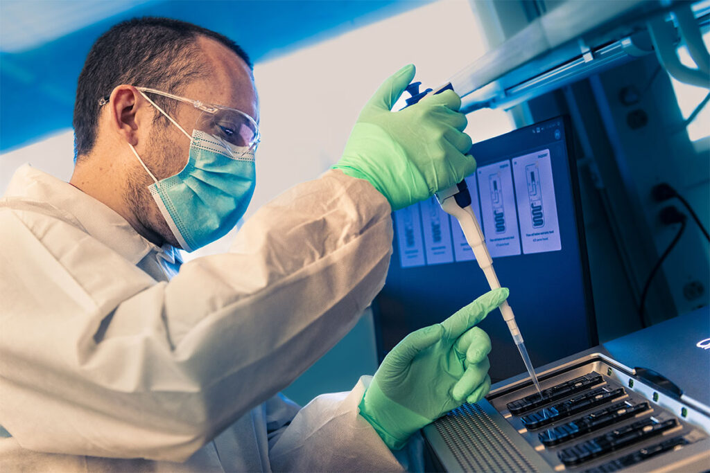 A scientist wearing protective mask, goggles and gloves uses a pipette to prepare samples.