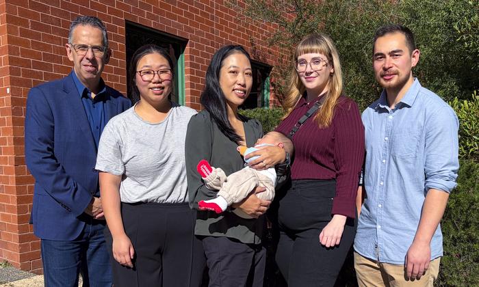 New Research Pinpoints Why Flu Turns Deadly in Pregnancy Five researchers, one holding her infant, stand outside the university facility.